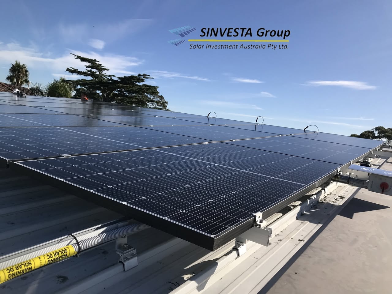 Rows of black solar panels installed by Sinvesta on a metal roof under a clear blue sky.