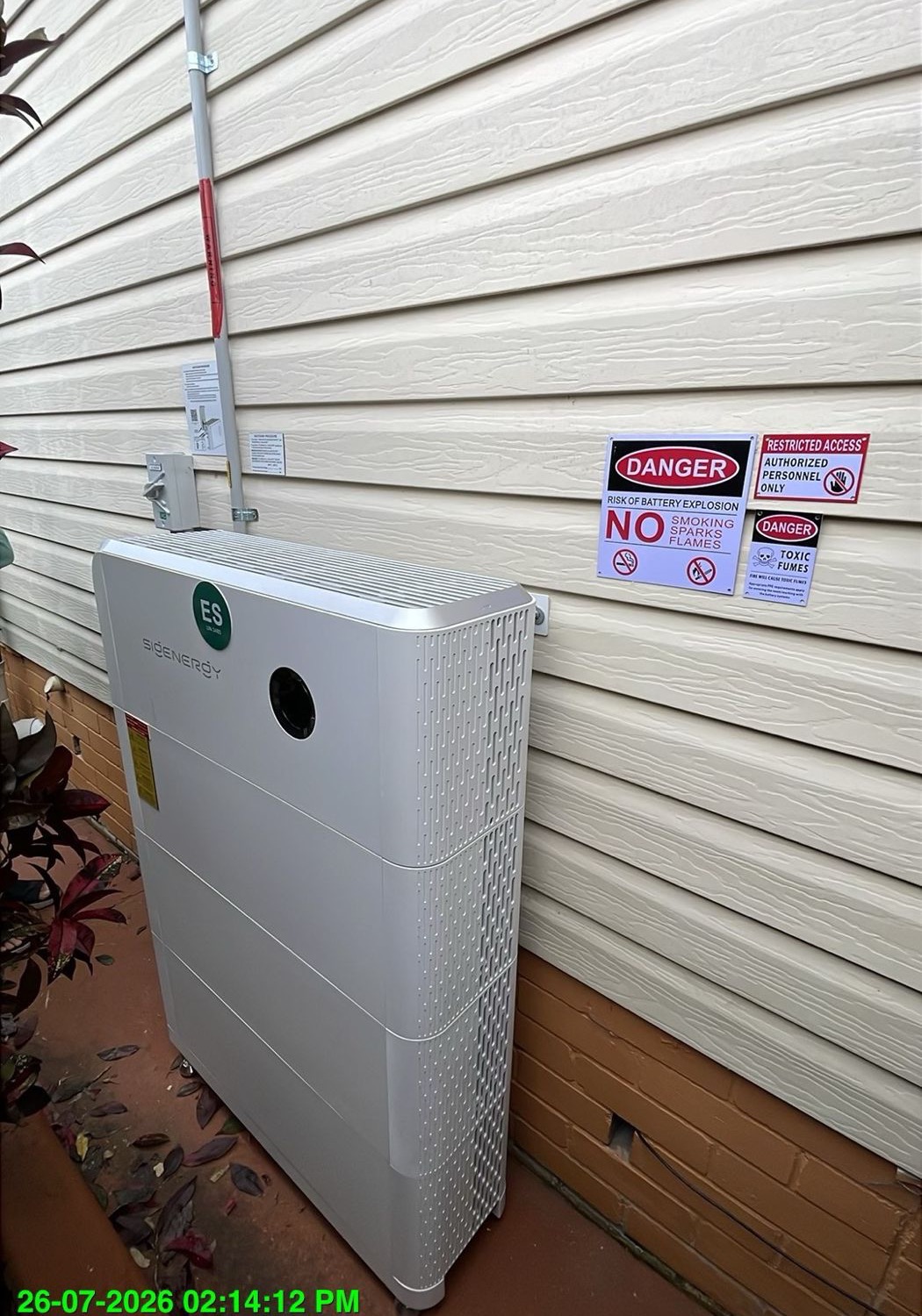Sigenergy SigenStor battery with three modules installed on a weatherboard wall, with an isolator, conduit and battery safety signage.