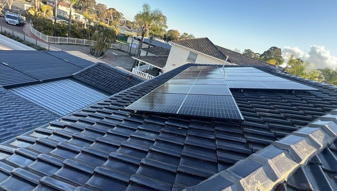 Solar panels installed on a dark tiled roof in a Sydney suburb, lit by late-afternoon sun.