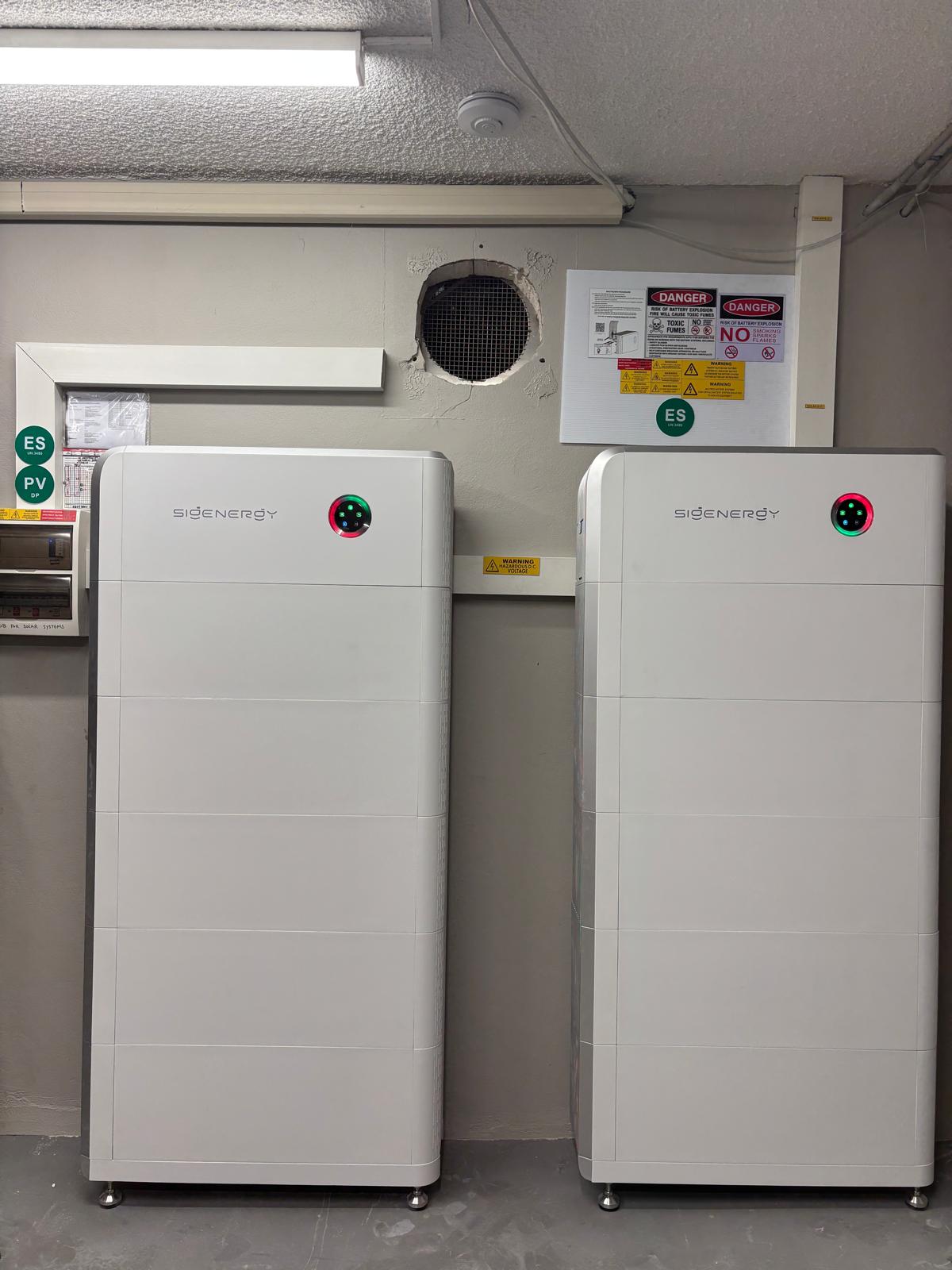 Two Sigenergy SigenStor units in a garage beside a switchboard labelled for the ES and PV circuits.